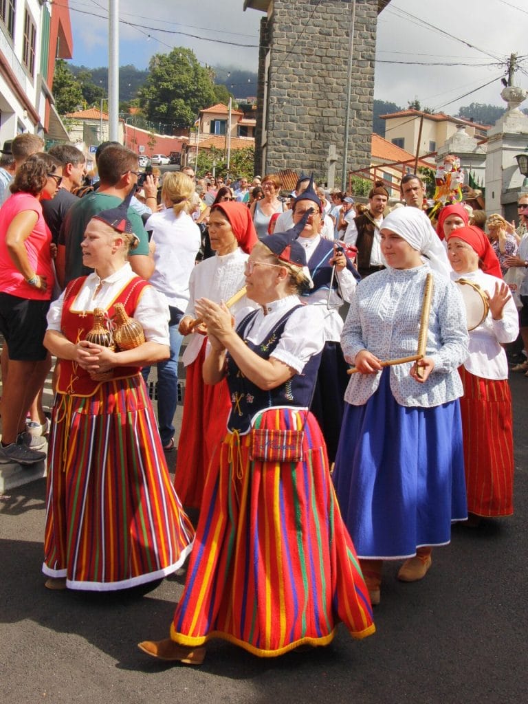 Frauen in farbenfroh gestreiften traditionellen Trachten gehen an einem Umzug auf der Strasse.