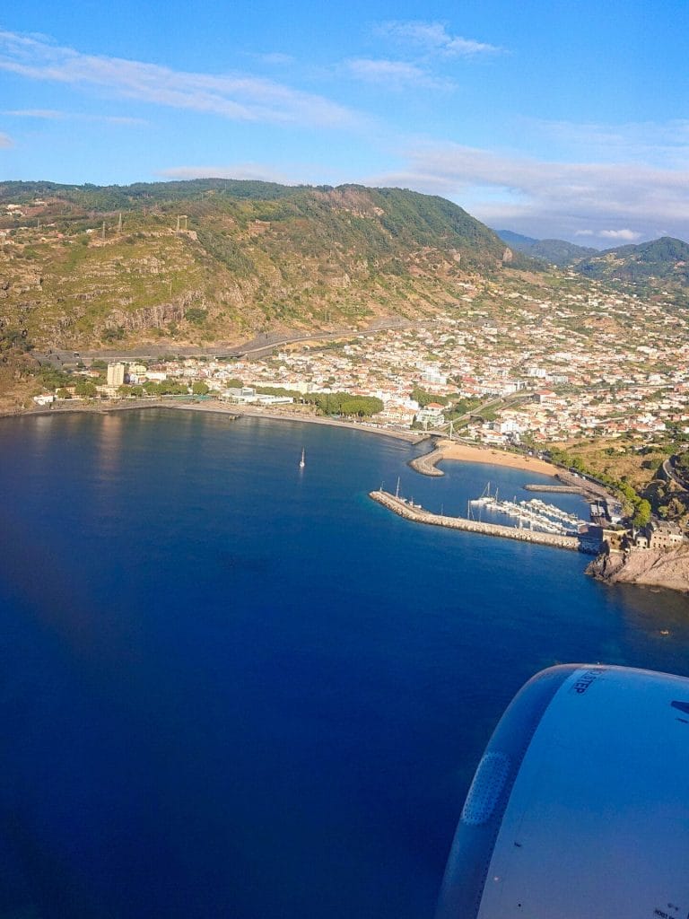 Luftbild beim Landeanflug auf die Insel Madeira mit Blick auf eine Meeresbucht, Hafen, Kleinstadt und Berge im Hintergrund