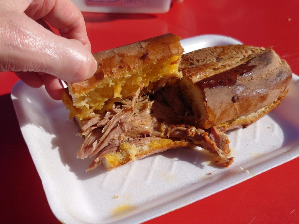 Nahaufnahme einer Hand, die ein mexikanisches Sandwich (Torta) öffnet und das saftige, gezupfte Fleisch Cochinita Pibil im Inneren zeigt, serviert als authentischen Street Food auf einem einfachen Teller.