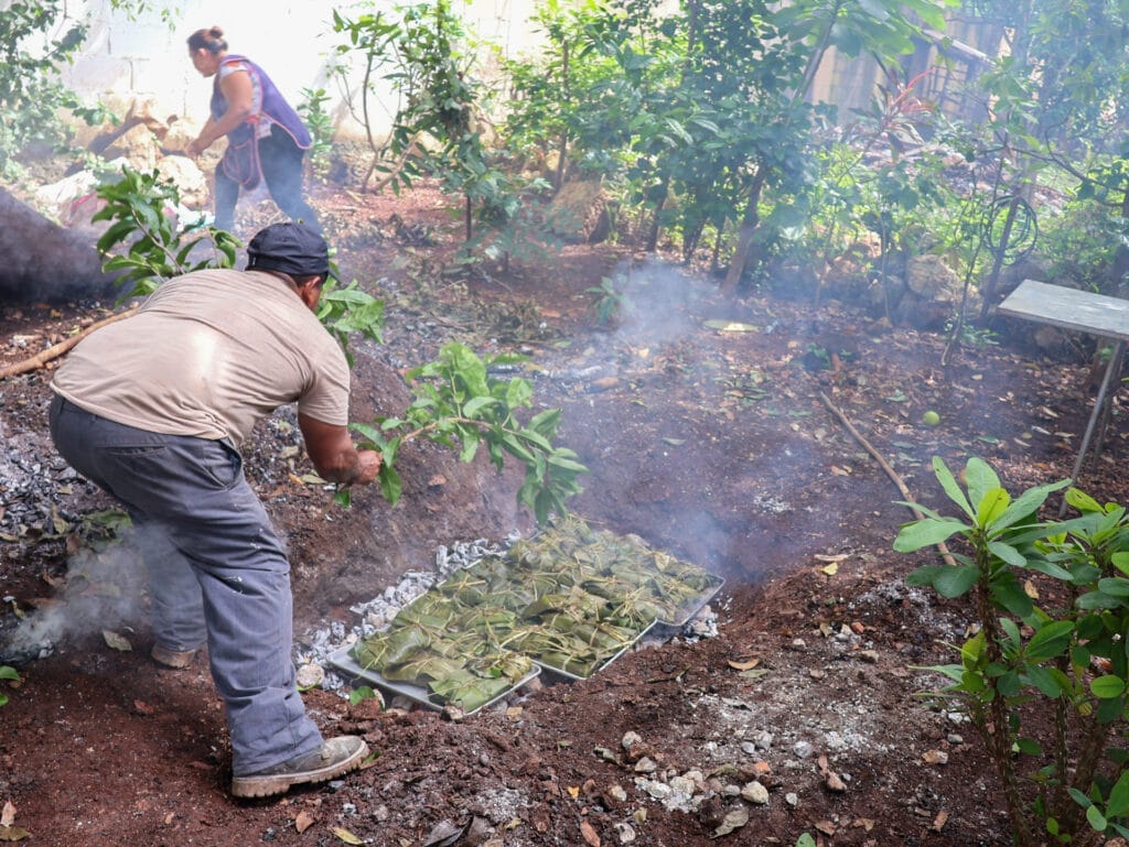 Einheimischer bereitet traditionelle, in Bananenblätter gewickelte Speisen in einem rauchenden Erdofen in Mexiko zu