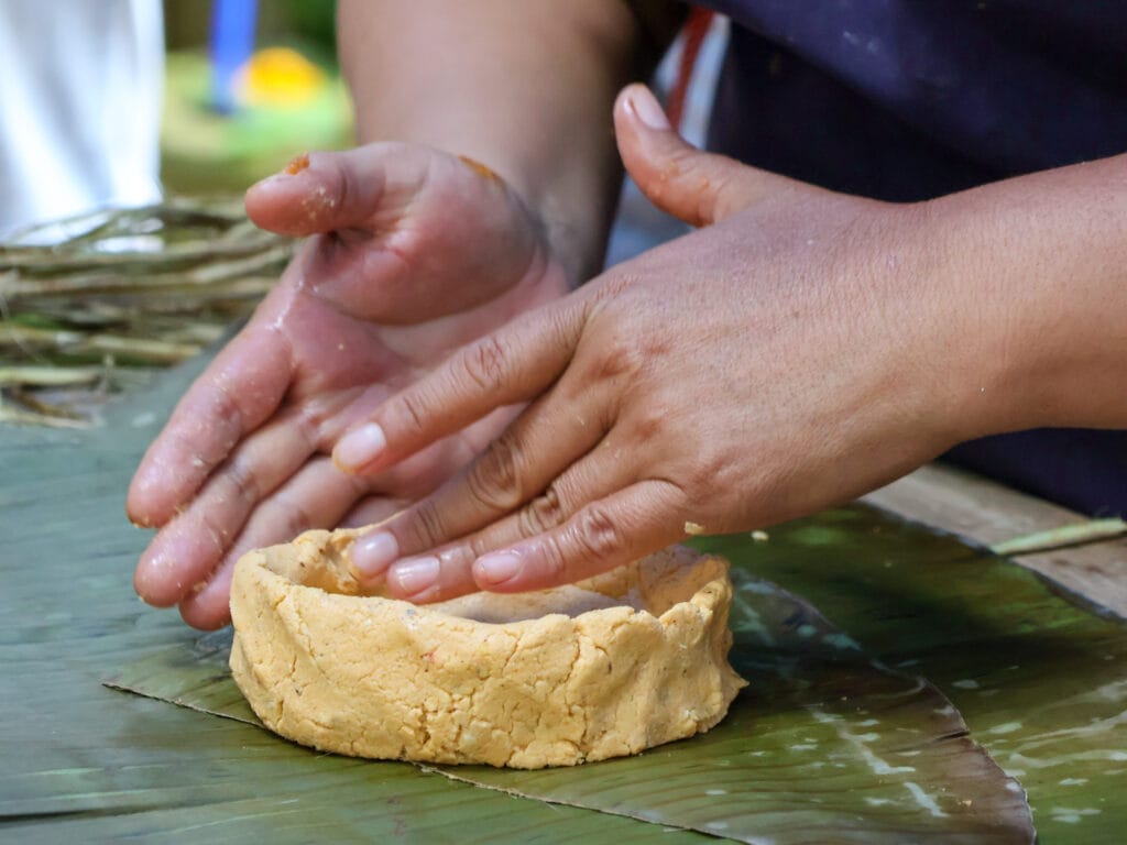 Nahaufnahme von Händen, die auf einem grünen Bananenblatt traditionellen Mais-Teig für das mexikanische Gericht Mukbilpollo formen