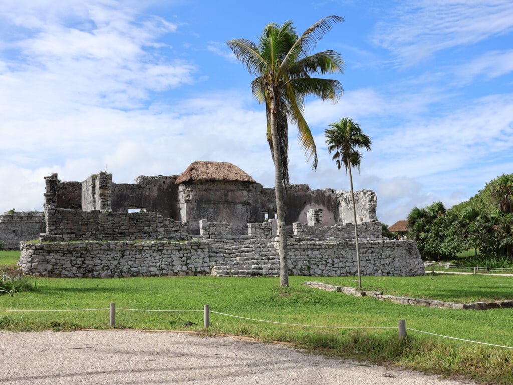 Historisches Steingebäude der Maya-Stätte Tulum in Mexiko mit Palmen und einer gepflegten Rasenfläche unter blauem Himmel